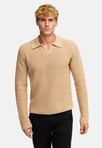 Strikket, beige genser med et teksturert mønster, V-hals og en kontrasterende krageutforming. Lange ermer og avslappet passform.