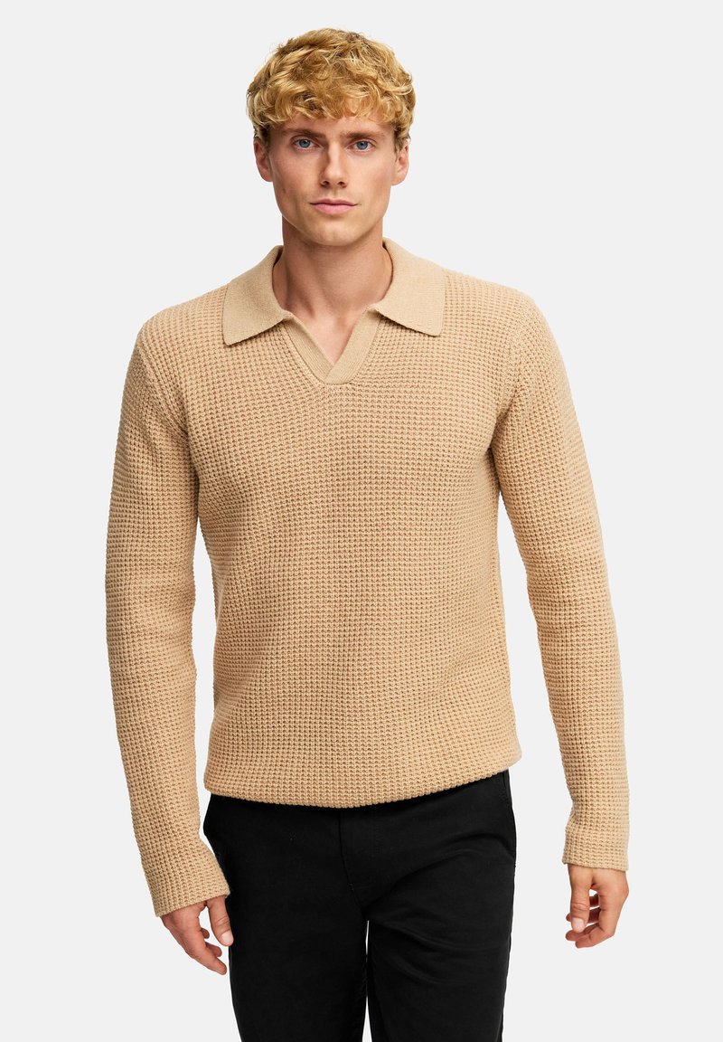 Strikket, beige genser med et teksturert mønster, V-hals og en kontrasterende krageutforming. Lange ermer og avslappet passform.