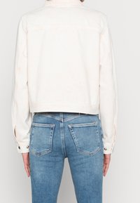 Vit denimjacka med en kortad design och synliga sömdetaljer. Parat med ljusblå jeans med en klassisk femficksstil.