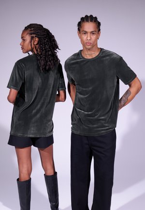 Donkergroene, fluwelen, T-shirts met korte mouwen en horizontale ribbels, gedragen met zwarte shorts en zwarte kniehooglaarzen, van voren en van achteren getoond.