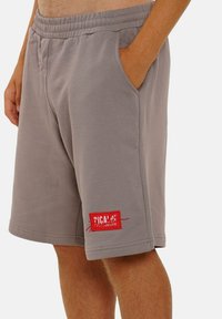 Gray cotton shorts with an elastic waistband, side pockets, and a red tag on the left leg featuring brand text and stitching details.