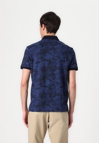 Granatowa koszulka polo z ciemnym wzorem kwiatowym. Krótkie rękawy i czarny kołnierzyk. Wykonana z miękkiego, teksturowanego materiału.