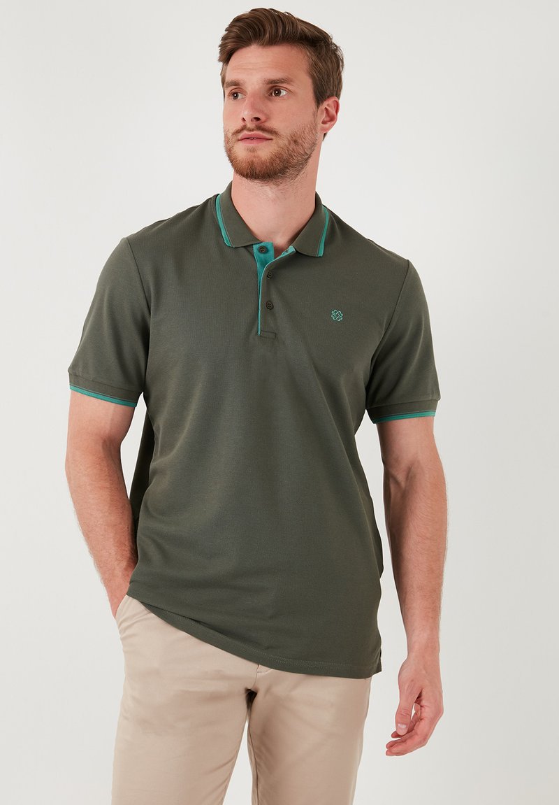 Olivno zelena polo majica s turkiznimi detajli, kratkimi rokavi, zapenjanjem na tri gumbe in diskretnim logotipom na levem prsnem delu. Mehka tekstura.