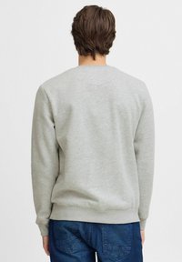 Sudadera gris con cuello redondo, mangas largas y puños de canalé. Textura de tela suave, combinada con jeans de mezclilla de un azul oscuro.