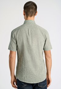 Krótki rękaw, jasnozielona strukturalna koszula z kołnierzykiem, z detalem plisy z tyłu i zaokrąglonym dołem, zestawiona z ciemnymi dżinsami.