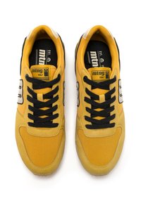 Un par de zapatillas amarillas y negras con cordones negros, logotipos laterales blancos y etiquetas "mtng 1967" en las lenguas, vistas desde arriba sobre un fondo blanco.