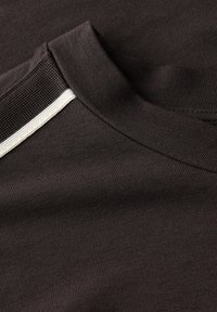 Schokoladenbraunes T-Shirt mit einem gerippten Kragen und einem diagonalen weißen Streifenakzent auf der Schulter. Weicher, strukturierter Stoff.