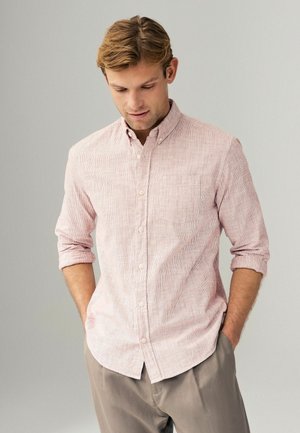 Light pink button-up shirt with a subtle striped pattern, short sleeves rolled up, and single chest pocket, paired with light gray trousers.