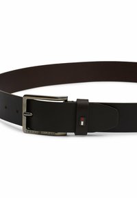 Une ceinture en cuir brun foncé avec une boucle en métal argenté. Elle présente un logo sur la boucle et un motif de couture soigné le long des bords.