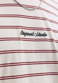 Biały bawełniany t-shirt z czerwonymi poziomymi paskami. Na przodzie haftowany napis "Originals Studio". Do zestawu dołączony srebrny łańcuszek.