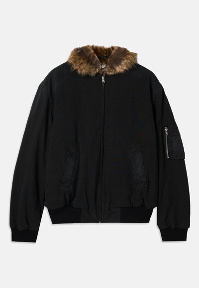 Juodas bomberio tipo švarkas su dirbtiniu kailio apykakle, guminėmis rankogaliais ir apačia, užtrauktuku užsegama kišene rankovėje bei šoninėmis kišenėmis patogiam daiktų laikymui.