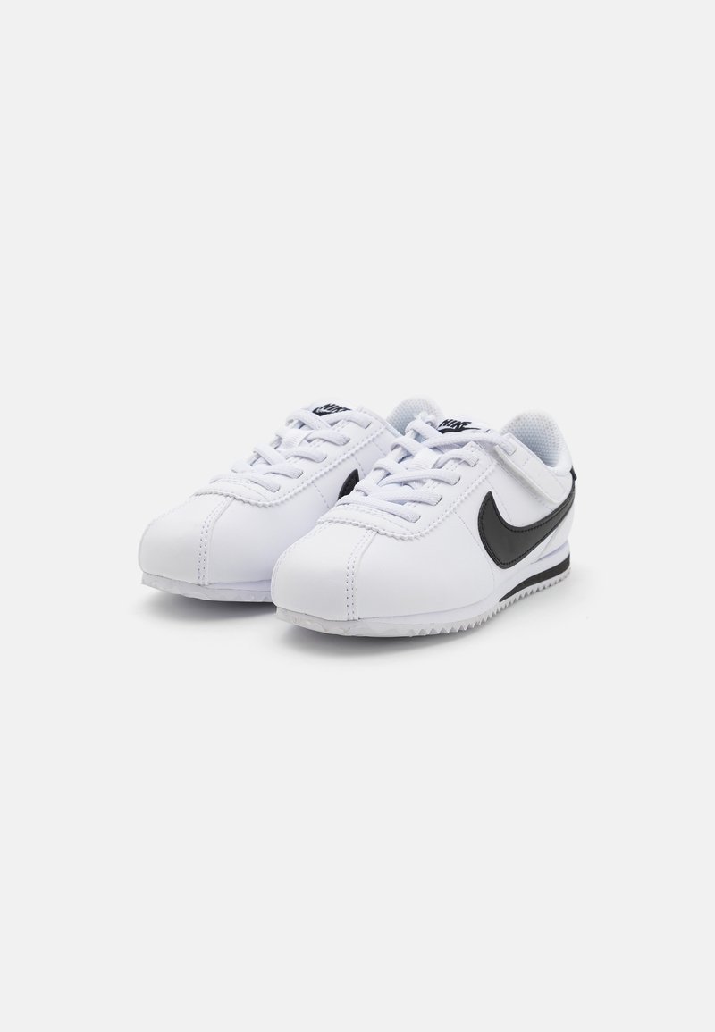 Zapatillas sintéticas blancas con un swoosh negro de Nike, cordones planos, cuello acolchado y suela de goma texturizada con un patrón en zigzag.