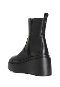 Botas negras hasta el tobillo con una suela plana y gruesa, hechas de cuero suave. Cuentan con una cremallera lateral y un lazo en el talón para facilitar su colocación.