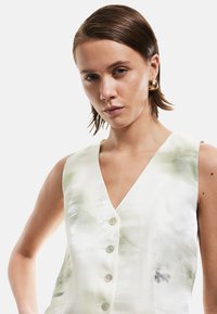 Ärmelloses, V-Ausschnitt-Kleid in Weiß mit grünen Aquarellmustern. Vier Knopfverschlüsse vorne, aus einem glänzenden Stoff gefertigt.