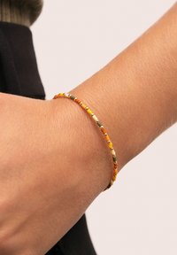 Pulsera de cuentas con cuentas circulares multicolores en naranja, amarillo, verde y dorado, colocada sobre una banda delgada y flexible, llevada en la muñeca.