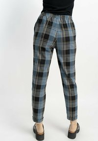 Spodnie w kratę w odcieniach niebieskiego, czarnego i beżowego z elastycznym pasem. Materiał wydaje się gładki, a krój jest luźny. Obecne płaskie kieszenie z przodu.