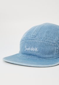 Casquette en denim bleu avec une visière plate et le texte blanc cousu "Just do it." à l'avant, présentant une texture lisse et un design classique à cinq panneaux.