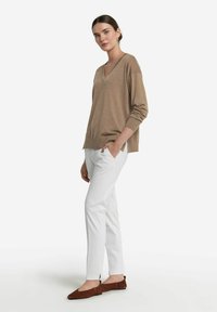 Ljusbrun v-ringad tröja med ribbade ärmar, i kombination med vita skräddarsydda byxor och bruna ballerina-skor, med en enkel och stilren design.