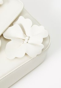 Sac à main en cuir blanc avec une finition texturée, présentant un grand accent floral fait du même matériau à l'avant, avec des accessoires en argent.