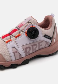 Chaussure de sport en mesh rose léger avec système Boa sans lacets, accents texturés et semelle extérieure en caoutchouc noir pour une meilleure traction.