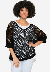 Schwarzer, offener Strickpullover mit Rautenmuster, weiten Ärmeln und einem weißen Unterhemd. Verfügt über einen runden Ausschnitt und eine horizontale Strickstruktur.