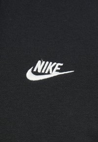 Juoda audinys su ribbine tekstūra, kuriame yra balto siuvinėto "NIKE" logotipo ir išlenktos swoosh formos.