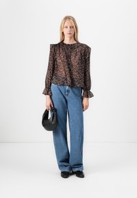 Blusa nera trasparente con motivi floreali, maniche a palloncino e colletto con volant, abbinata a jeans larghi blu chiaro e una borsa nera.