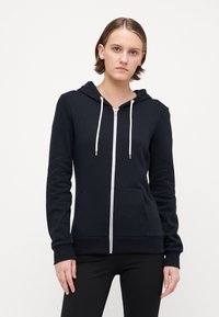 Svart hettegenser med hvite snorer, sidelommer og ribbede ermer. Laget av myk materiale, med et minimalistisk design.