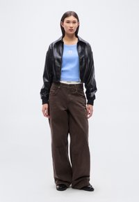 Μαύρο κοντό μπουφάν από συνθετικό δέρμα, ανοιχτό μπλε εφαρμοστό τοπ, φαρδιά καφέ παντελόνια και μαύρα παπούτσια. Το μπουφάν διαθέτει κλείσιμο με φερμουάρ και ριμπ μανσέτες.