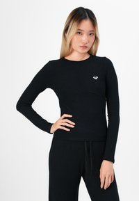 Black long-sleeve top in ribbed texture, featuring a round neckline and a logo accent on the left side, paired with matching ribbed pants.