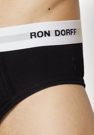 Črne bombažne kratke hlače z belim elastikom v pasu, na katerem je zapisano "RON DORFF" v črni barvi. Vsebujejo dvojne šive in minimalne oblikovne podrobnosti.