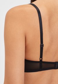 Sostén negro con tirantes ajustables, detalles de malla y una banda trasera lisa. La tela parece texturizada y se ajusta al cuerpo.