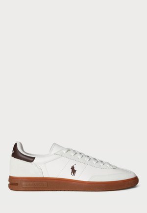 White low-top sneaker with a textured leather upper, brown accents on the heel, and a rubber sole. Features embroidered logo on the side.