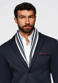 Blazer de lana azul marino con cuello de chal a rayas blanco y azul marino, superpuesto a una camisa blanca. Pañuelo rojo en el bolsillo del pecho.