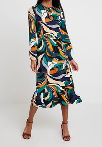 Sukienka z długim rękawem, dopasowaną talią, rozszerzającym się dołem i wielokolorowym wzorem w spirale w odcieniach zieleni, pomarańczu, fioletu i beżu. Lekki materiał.