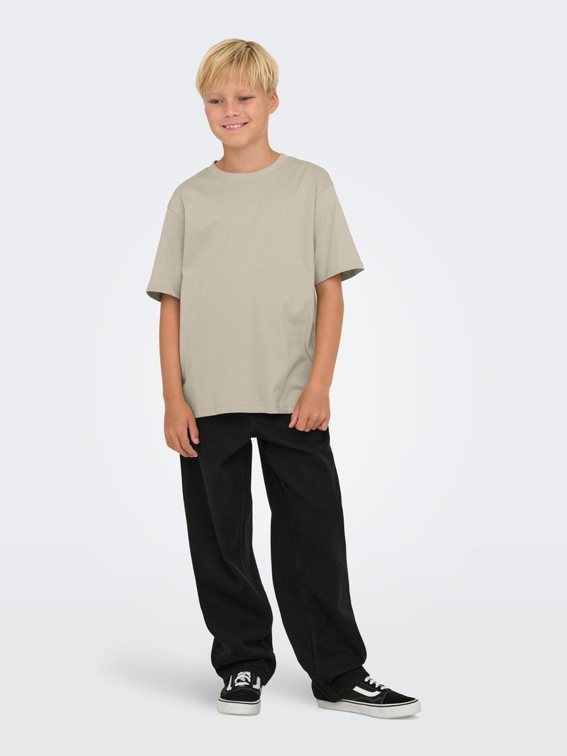 Lys beige t-shirt med korte ærmer, parret med løse sorte bukser. Optræden har en afslappet pasform og er komplementeret af sorte sneakers.