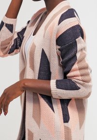 Stickad cardigan med geometriska mönster i rosa, beige och marinblå. Öppen framsida med långa ärmar och strukturerad tyg.