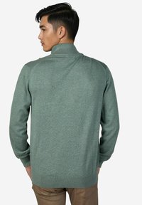 Grüner Strickpullover mit hohem Kragen, gerippten Bündchen und Saum sowie Raglanärmeln, zeigt eine glatte Textur und gleichmäßige Farbe.