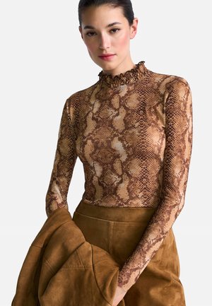 Long-sleeve, fitted top featuring a brown snake print pattern, with a ruffled mock neck and smooth texture. Paired with a brown suede jacket.