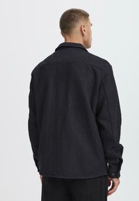 Black corduroy overshirt with a collar, featuring long sleeves, button cuffs, and a textured pattern on the fabric.