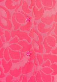 Różowa bluzka z teksturowanym wzorem kwiatowym, o gładkim wykończeniu i zapięciem na guziki w dopasowanym odcieniu różu.