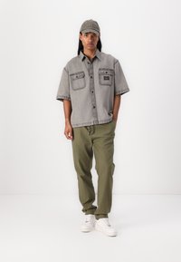 Grau Denim Kurzarmhemd, zwei Fronttaschen; olivgrüne Hose, taillierte Passform; weiße Turnschuhe; graue Mütze mit "Won" Stickerei.