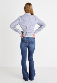 Chemise rayée à manches longues avec un col, associée à un jean évasé bleu marine. La chemise présente un design torsadé à l'arrière, et le jean est équipé de poches arrière.