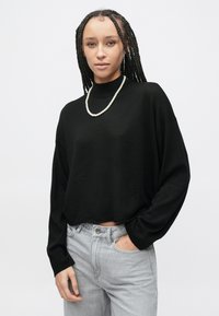 Pullover nero corto con collo alto, maniche larghe e trama morbida, abbinato a jeans grigio chiaro. Completo di una collana di perle.