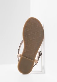 Sanda con suela marrón claro que presenta un patrón de logotipos de "Pepe Jeans London", correas beige y una hebilla plateada, fotografiada contra una esquina blanca.