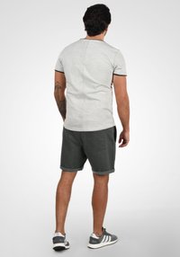 T-shirt gris clair avec un col rond et des bordures noires, associé à un short gris foncé. Le short a un ourlet roulé et une poche arrière.