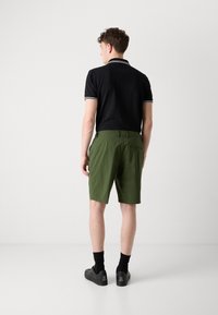 Polo noir avec des accents blancs, associé à un short vert olive. Le modèle porte des baskets noires et des chaussettes noires de longueur classique. Design simple.