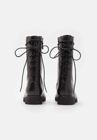 Bottes chevilles en cuir noir avec bouts ronds, laçage frontal et semelles en caoutchouc plates. Présentent des coutures visibles et des lacets foncés contrastants.