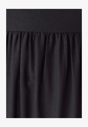 Melnas audums ar salocījumiem zem gludas jostas, parādot teksturētu auduma struktūru un mīkstus salocījumus.