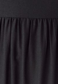 Černá látka se shromážděnými sklady pod hladkým pasem, ukazující texturovanou vazbu a jemné záhyby.